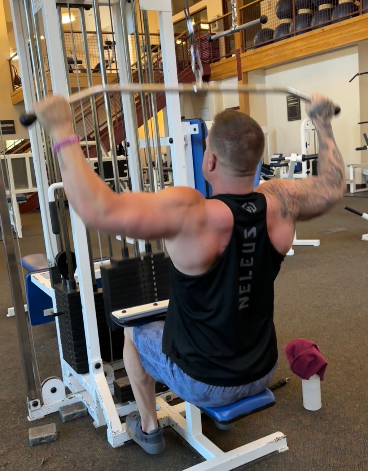 Man performing a lat pulldown exercise on a machine in a gym setting.