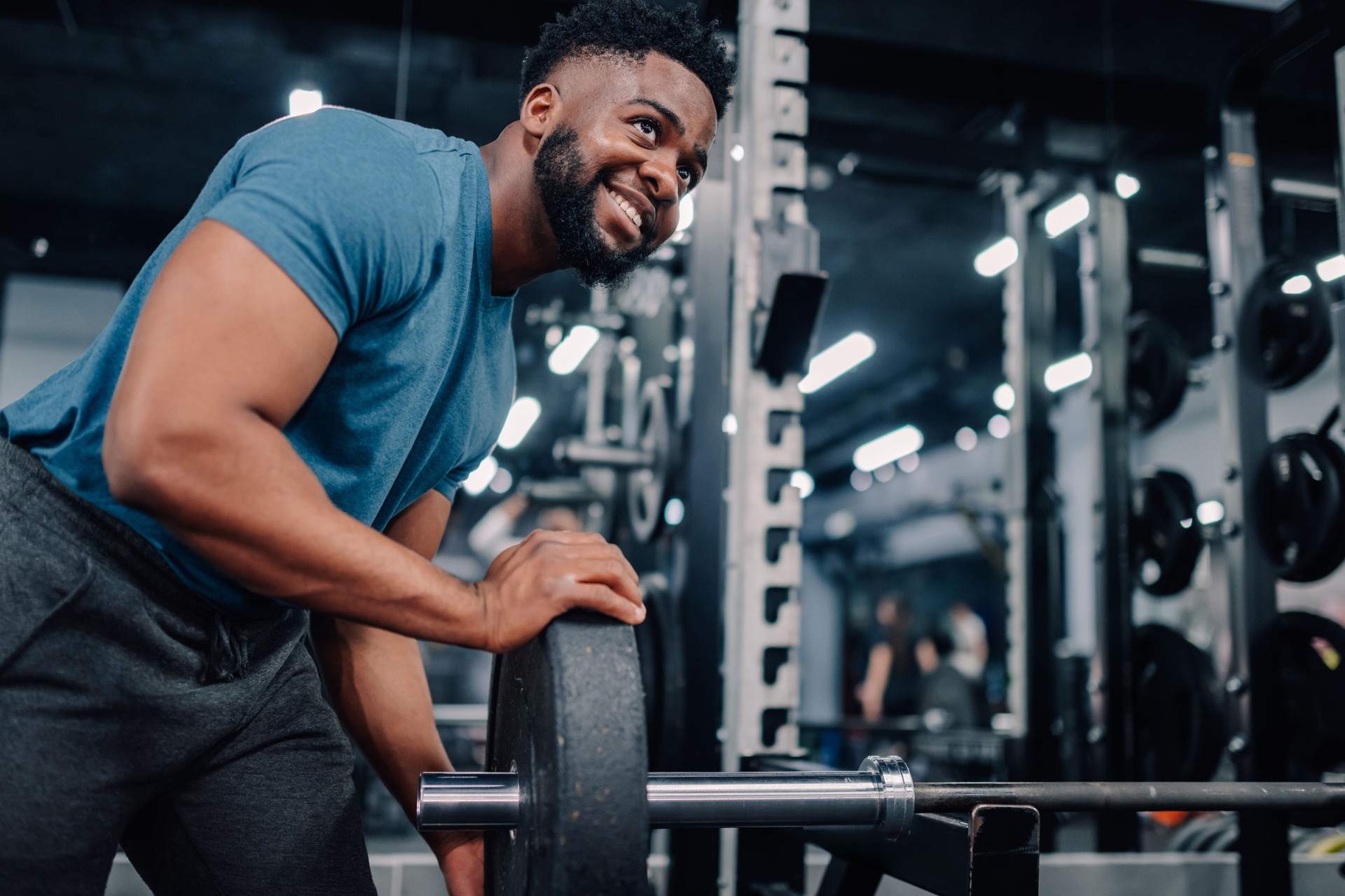 Young male athlete adding weights to barbell in gym