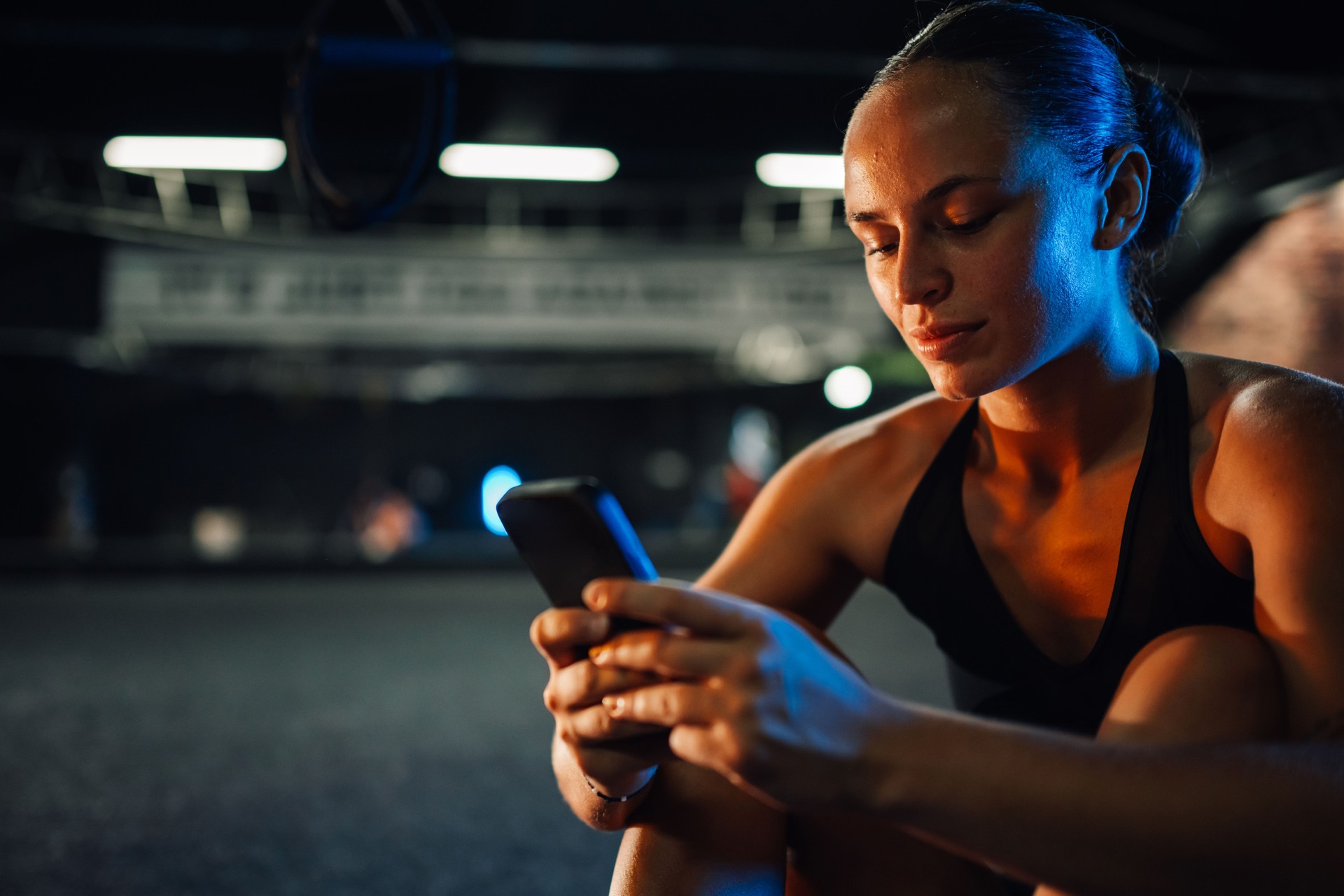 Focused female athlete using smartphone at the gym after evening workout